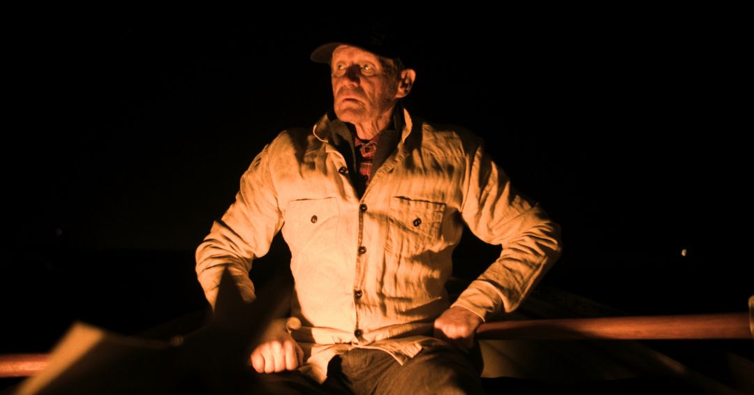 An older man in a pale jacket illuminated against the darkness, from A megváltó